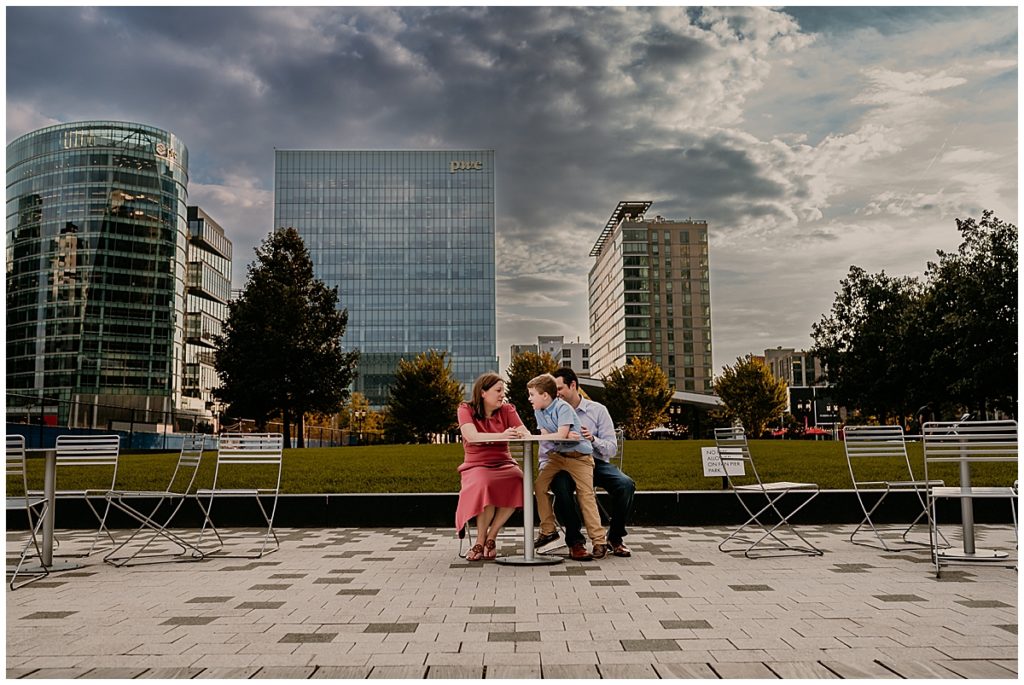 Family sitting at a table with city buildings and green grass in background.
