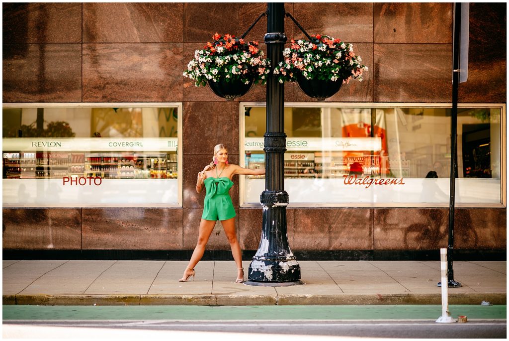 Girl wearing green jump suit on a light post for her Boston Senior Pictures.