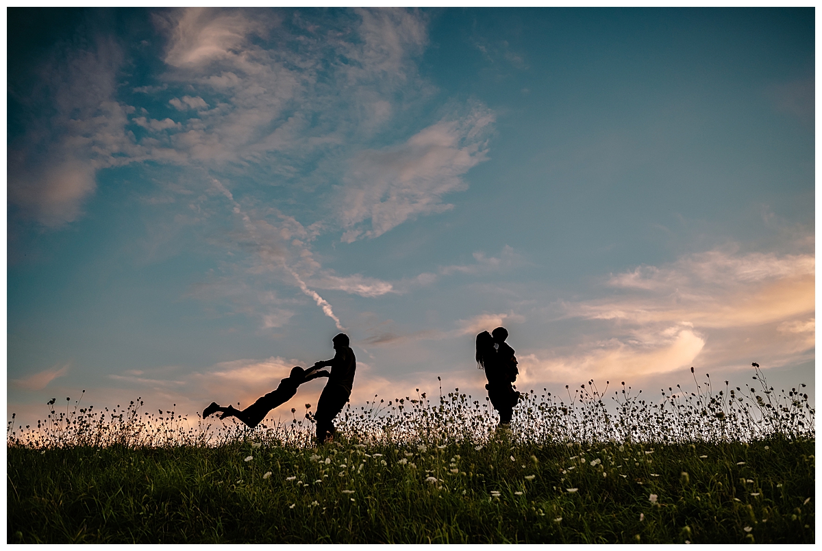 Boston family in a field dancing, silhouetted by the sun.
