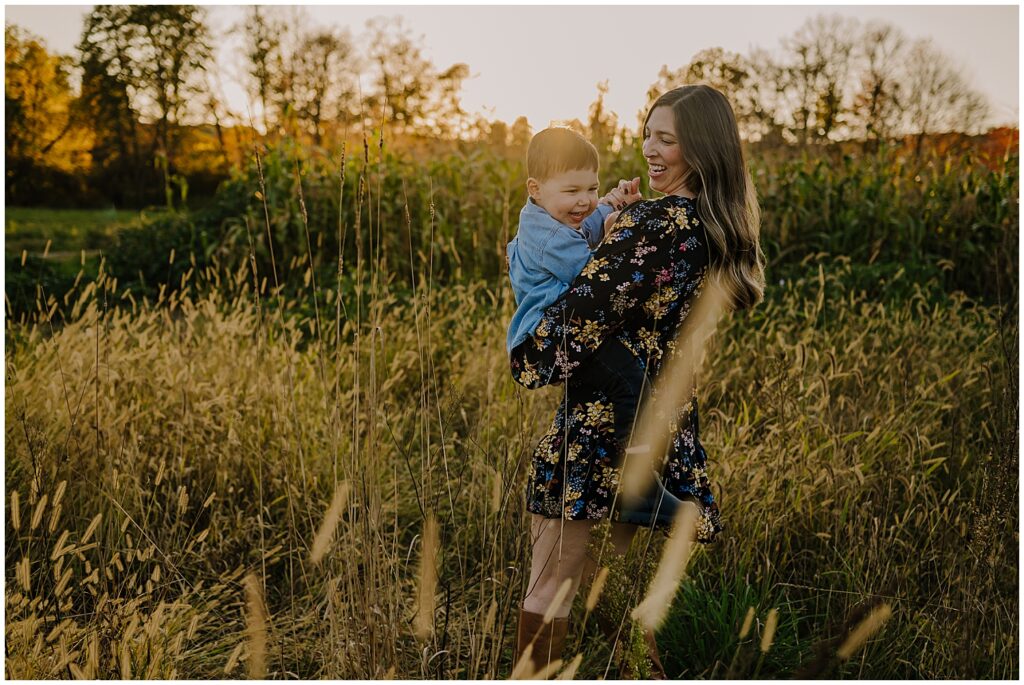 Mother holding her son dancing in a field with the sun behind them