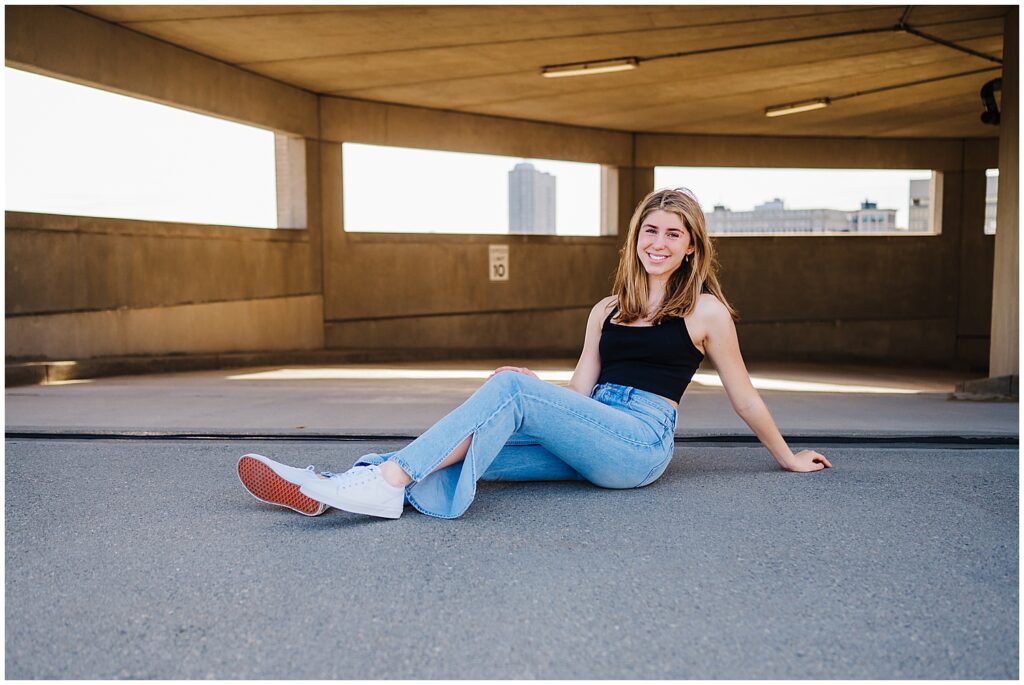 Girl sitting in a parking garage floor posing for Senior Photos in Boston.