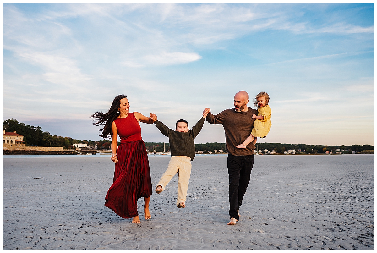 Family walking on the beach during golden hour. The father is holding the daughter and they are swinging their son.