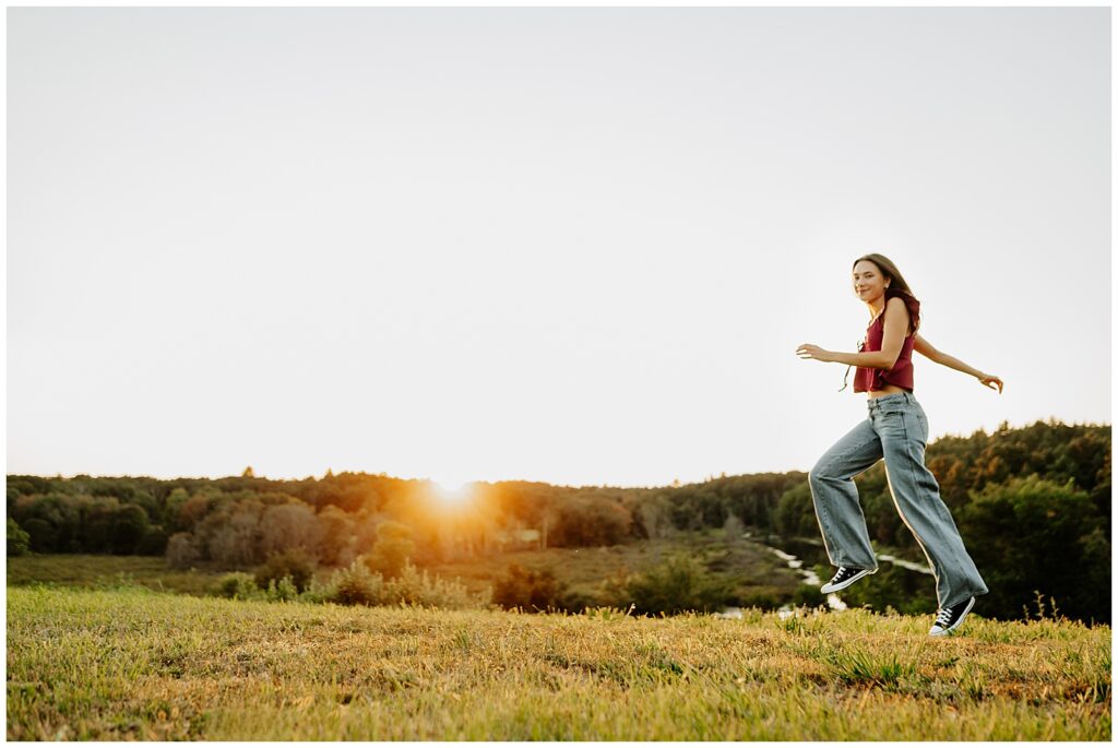 A Hopkinton senior skipping across a field with the sun setting behind her