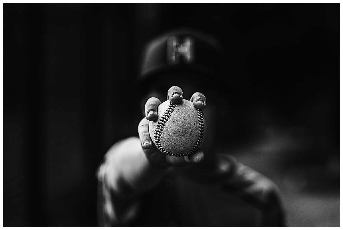 Black and white image of a boy holding a baseball in focus at the camera.