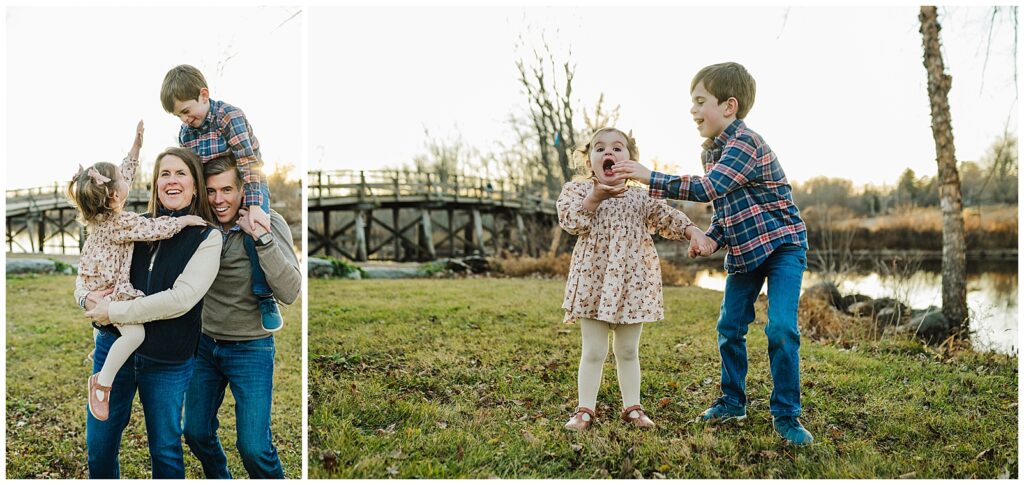 A father with his son on his shoulders and a mother carrying her daughter laughing. They are standing next to a river with a bridge in the background.