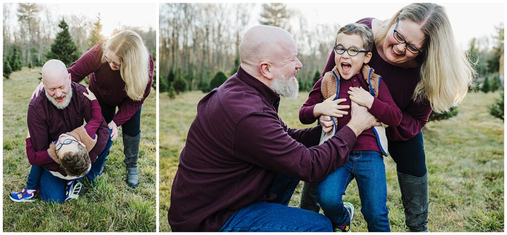 A father and mother tickling their son who is wearing fun blue glasses. The parents and son are wearing burgendy sweaters and jeans and are at a tree farm.