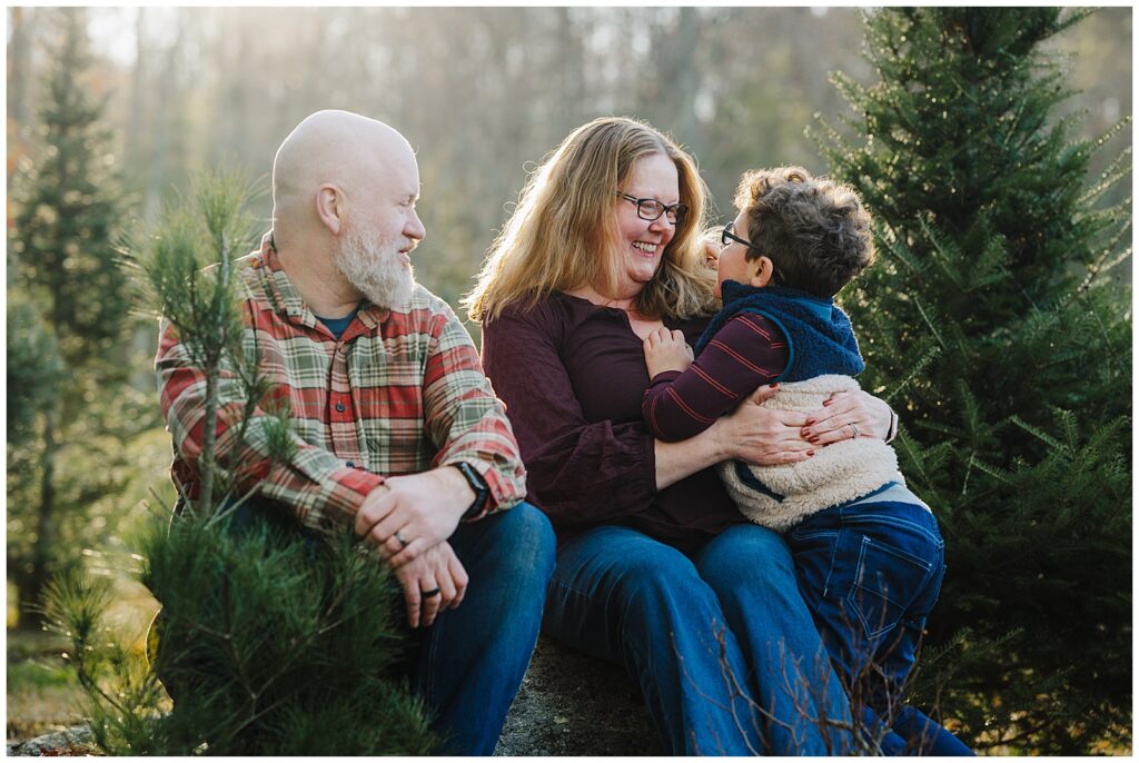 mother and father sitting on a log with their son cuddled up and smiling