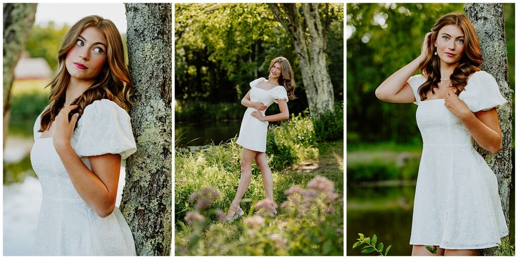 Senior girl in a white dress posing by a tree and holding a bouquet of flowers at sunset during an outdoor senior portrait session.