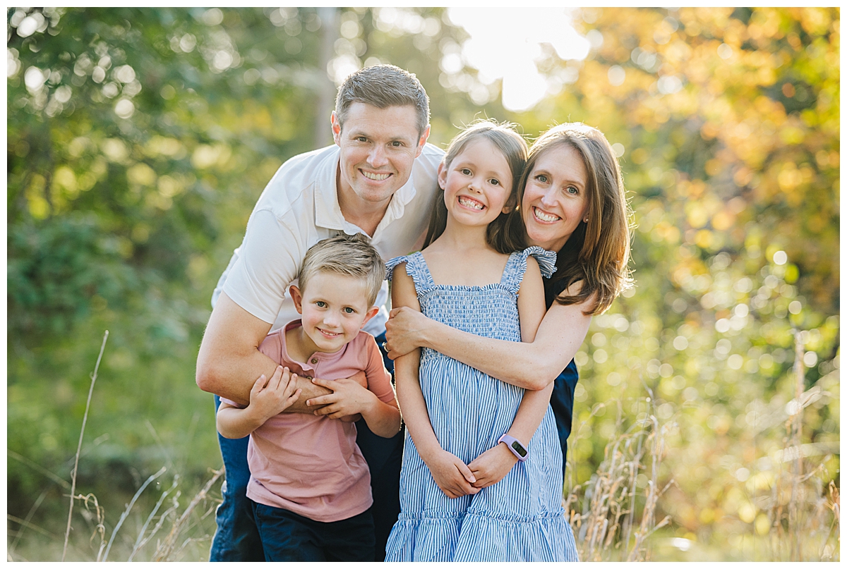 Natural posed family portrait with everyone smiling at camera during an outdoor session in MetroWest MA