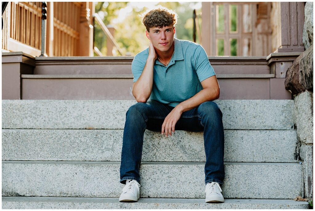 Senior boy seated on wide stone steps outside a historic building in Milford during golden hour senior portraits.