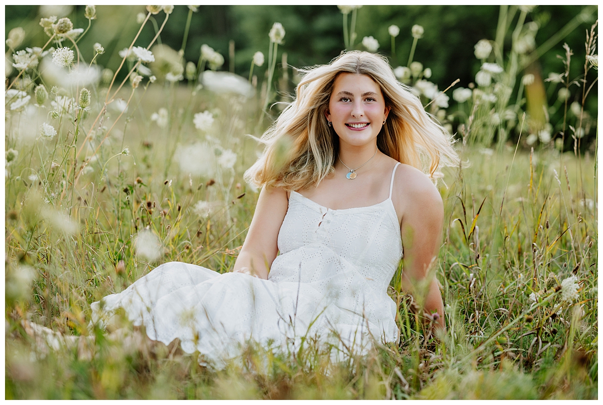 Senior wearing white dress sitting in a field after doing great senior picture prep.